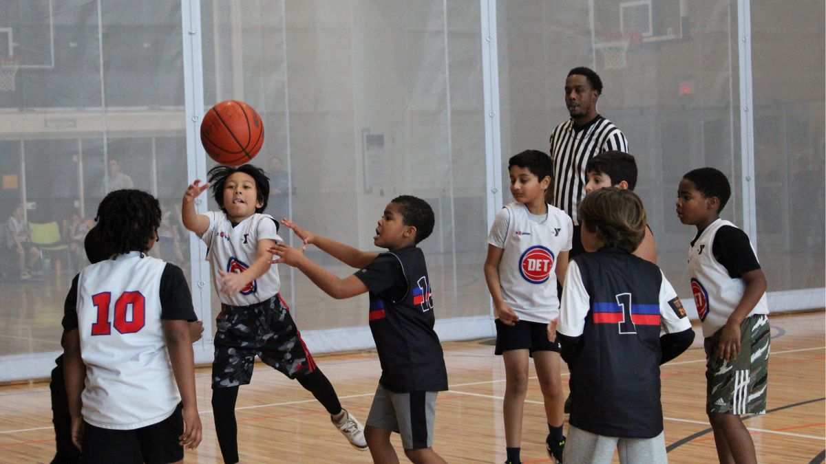 Children with a volunteer referee playing basketball in a sports program at the YMCA