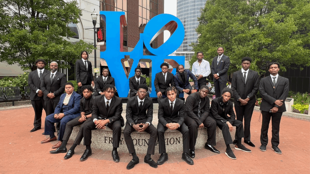 a group of teenage boys dressed in suits standing in front of a sculpture of the word LOVE