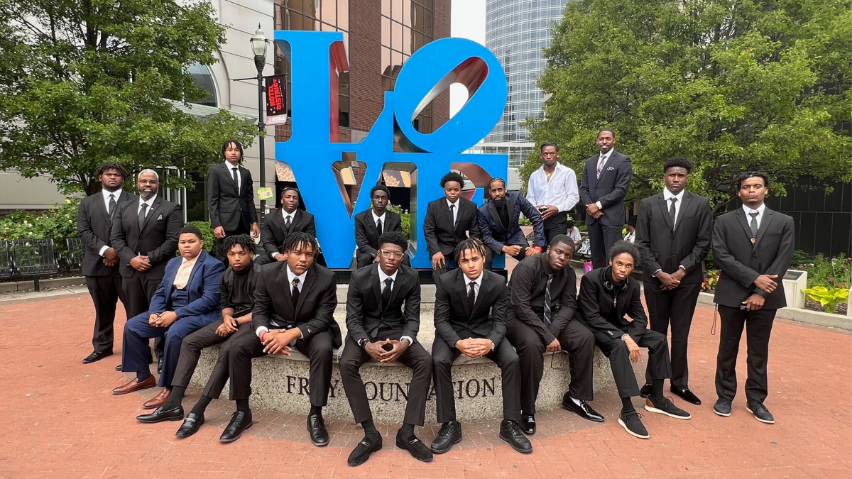 a group of teenage boys dressed in suits standing in front of a sculpture of the word LOVE