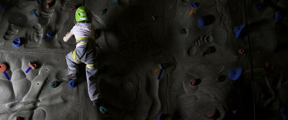 a youth climbing program participant on an indoor climbing wall at the YMCA