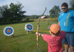 a photo of a kid practicing bow and arrow with a big guy in blue shirt
