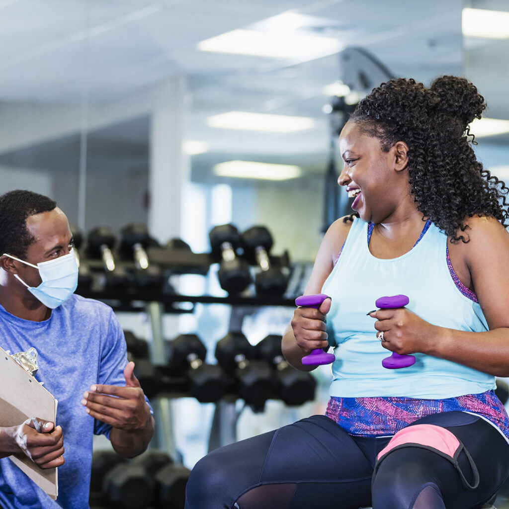 Wellness and Personal training at the Y - a photo of a man and woman conversing inside a gym while exercising