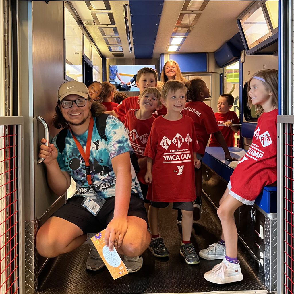 Kids smiling with a counselor during a YMCA Day Camp field trip to the Detroit Science Center
